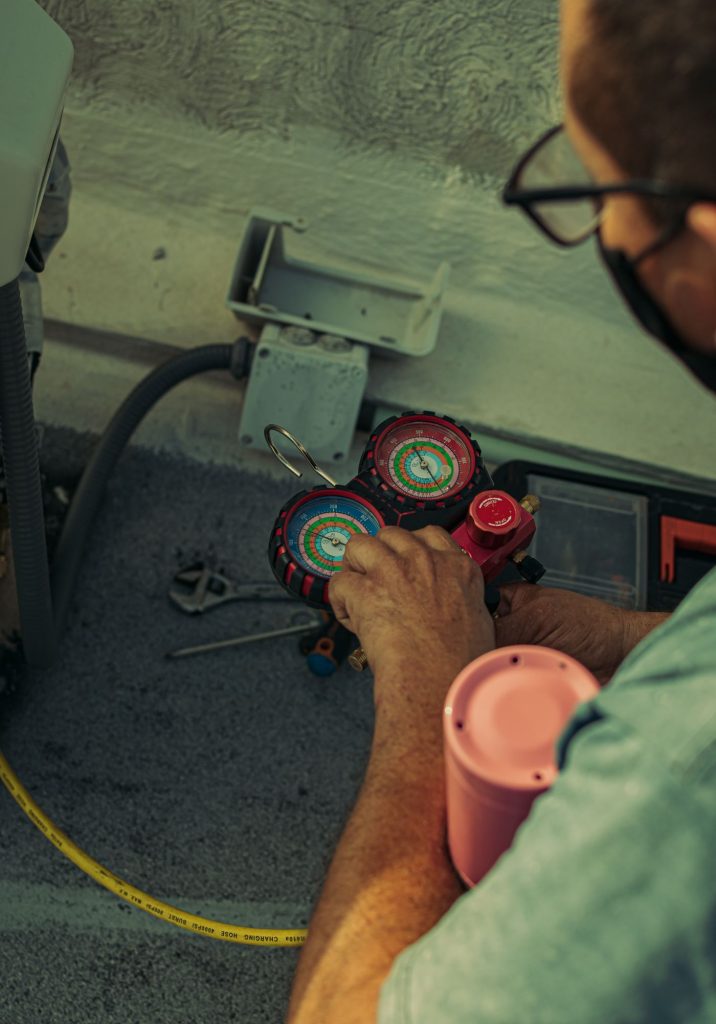 Technician adjusting a refrigerant manifold gauge while checking AC gas pressure