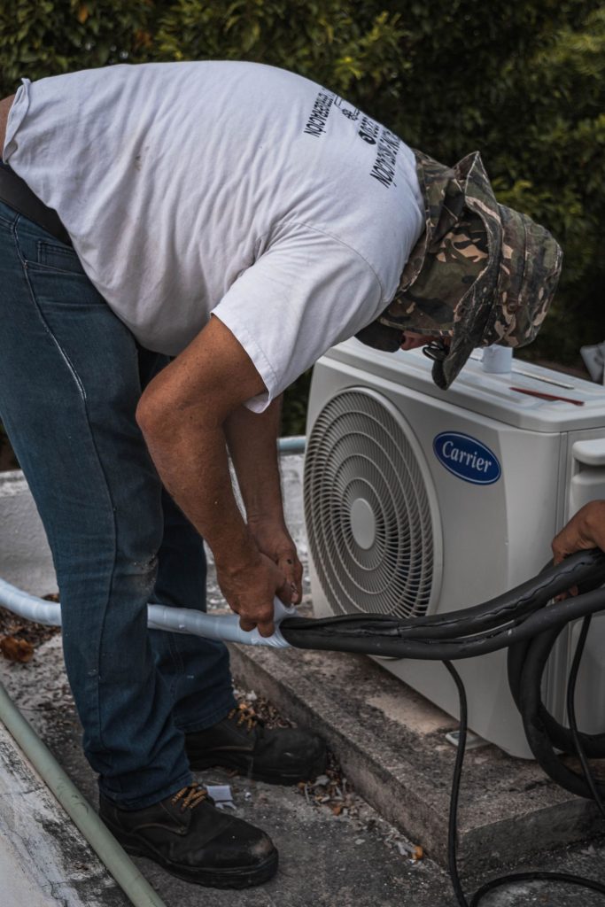 Technician connecting service hoses to an outdoor AC unit during maintenance