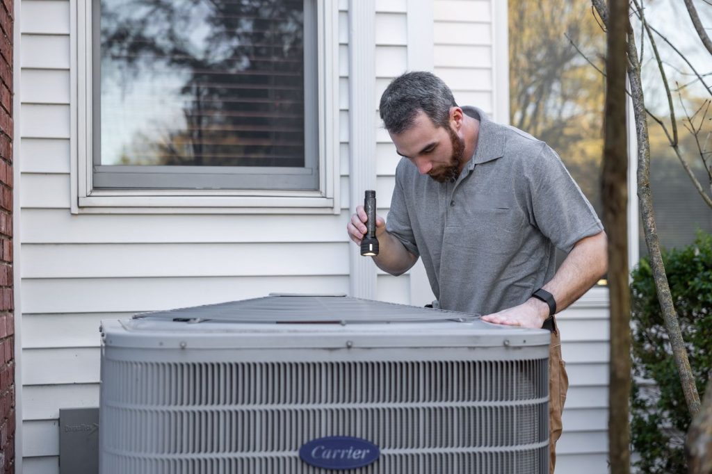 Technician inspecting an outdoor AC condenser unit beside a house