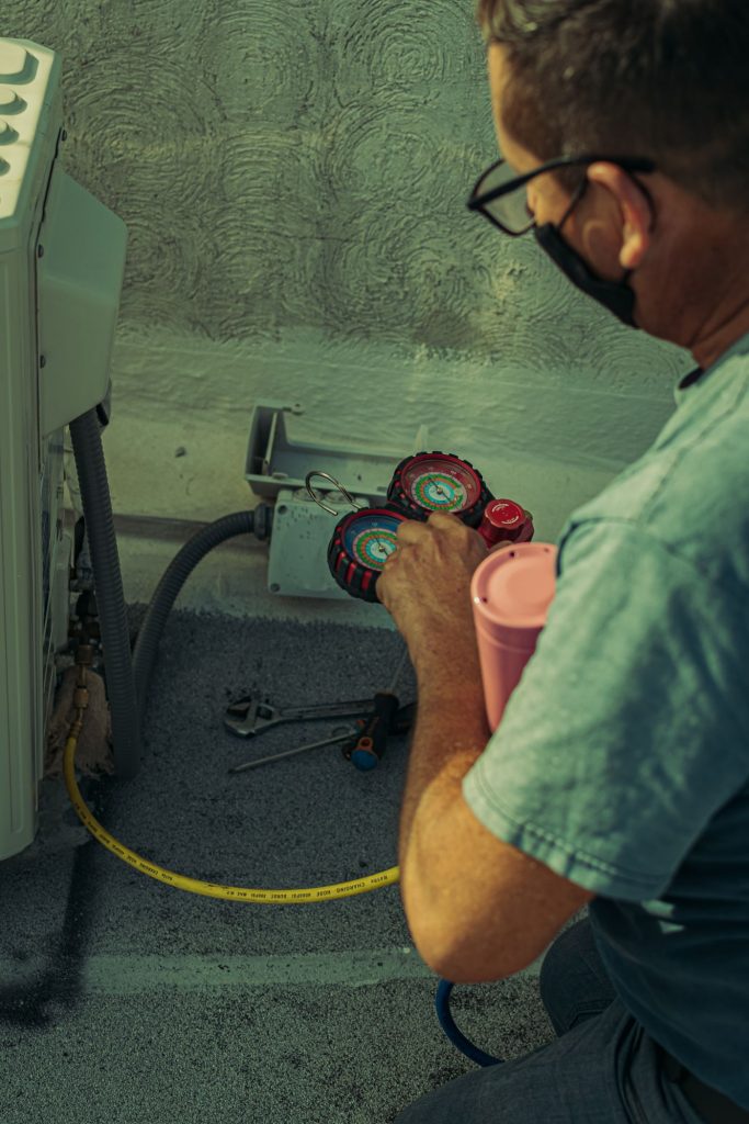 Technician checking an outdoor air conditioning unit with gauges and tools