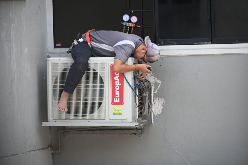 Technician working on an outdoor AC unit mounted on a building wall