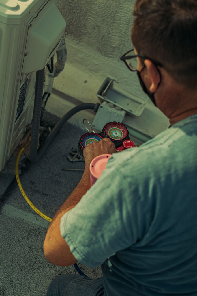 Technician repairing an outdoor air conditioning unit with gauges and tools