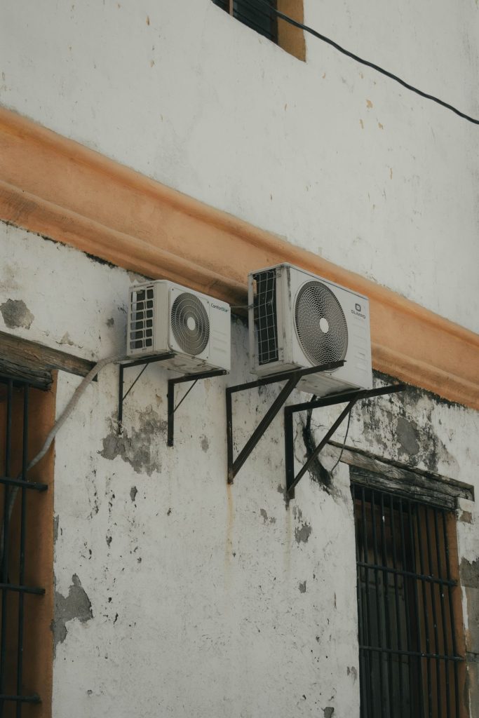 Two outdoor AC condenser units installed on brackets on a concrete wall